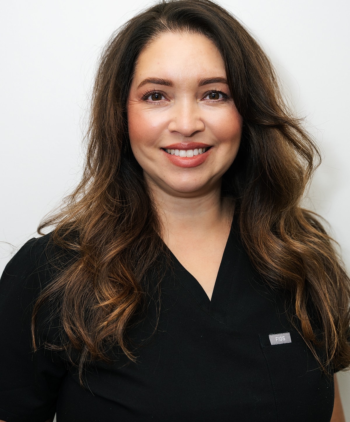 Smiling woman in black scrubs against beige background.