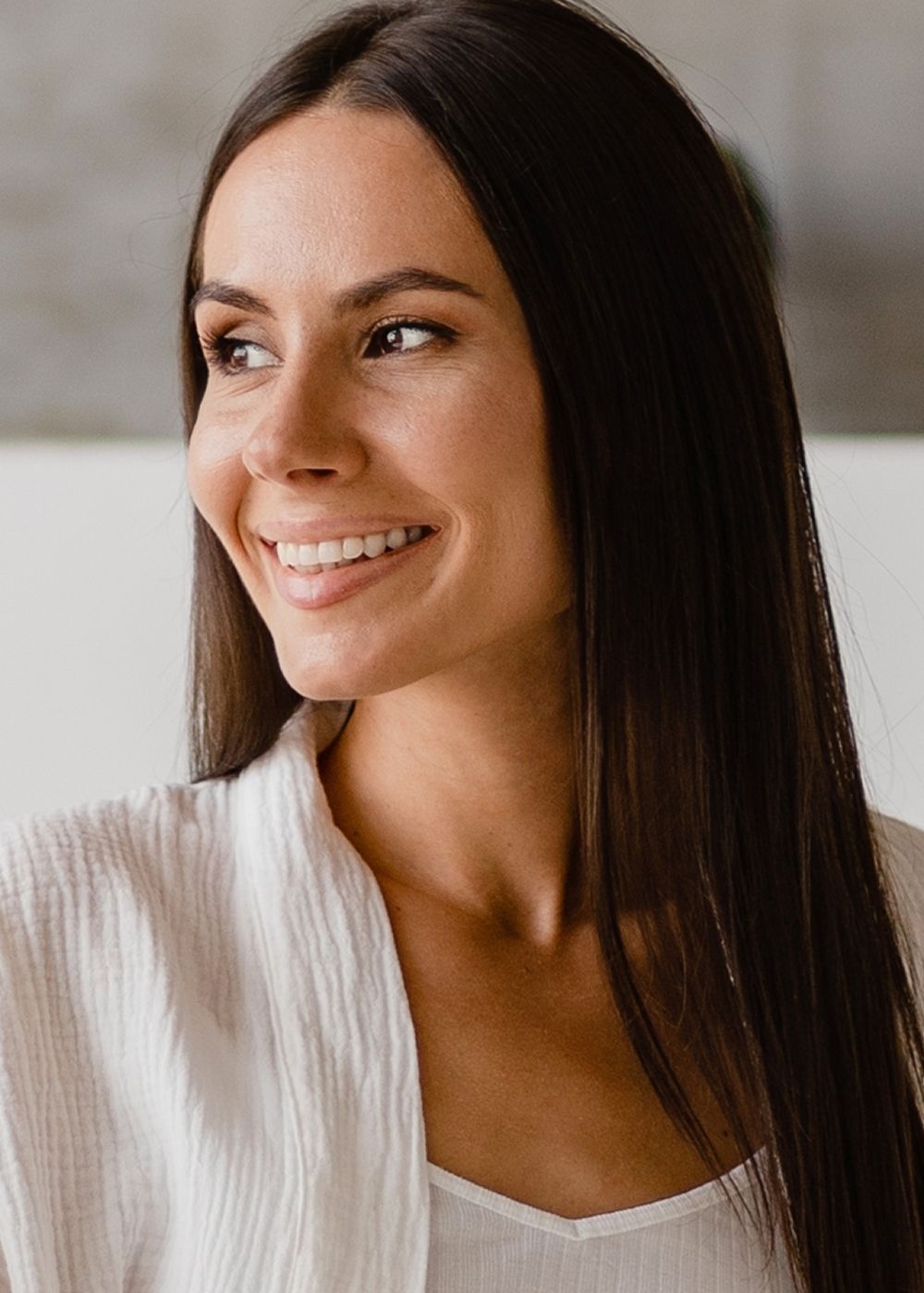 Smiling woman in a white outfit, soft background.