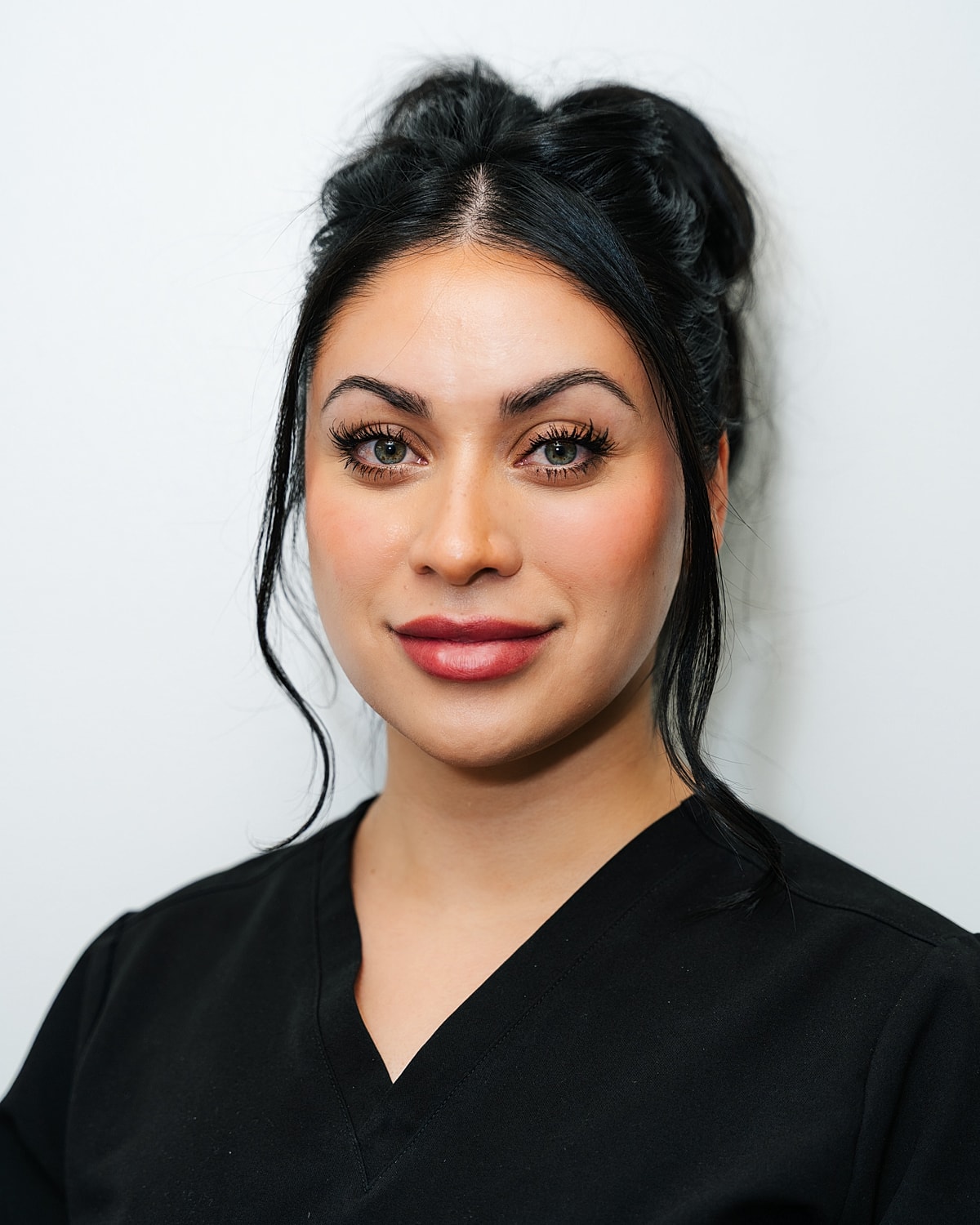 Woman in black scrubs posing against white background.