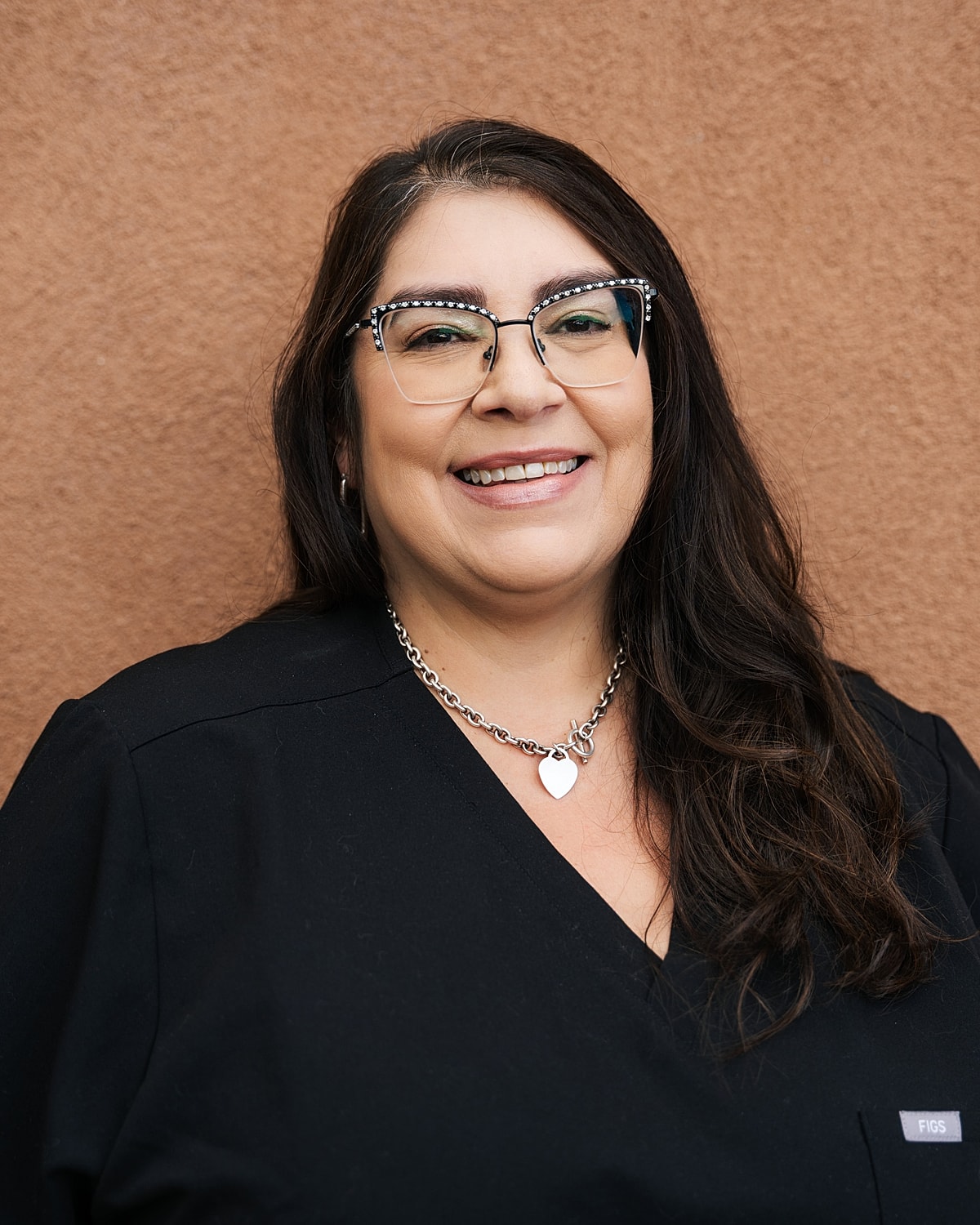 Smiling woman in black outfit against brown background.