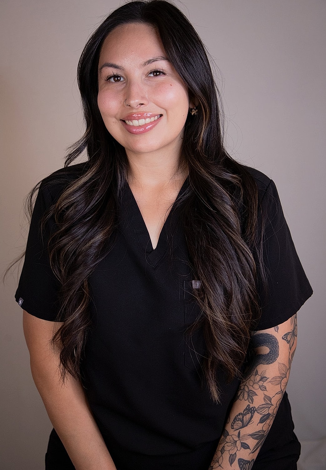 Person smiling in black scrubs against beige background.