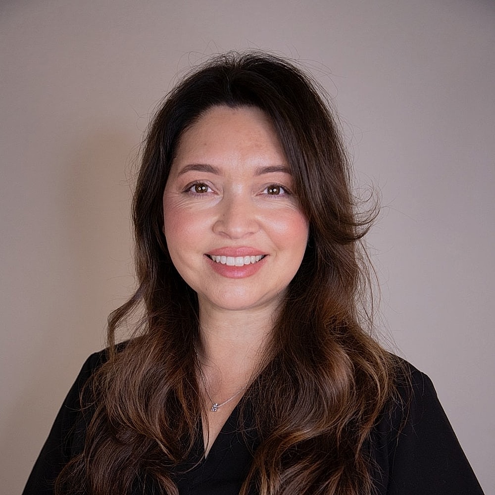 Smiling woman in black scrubs against beige background.