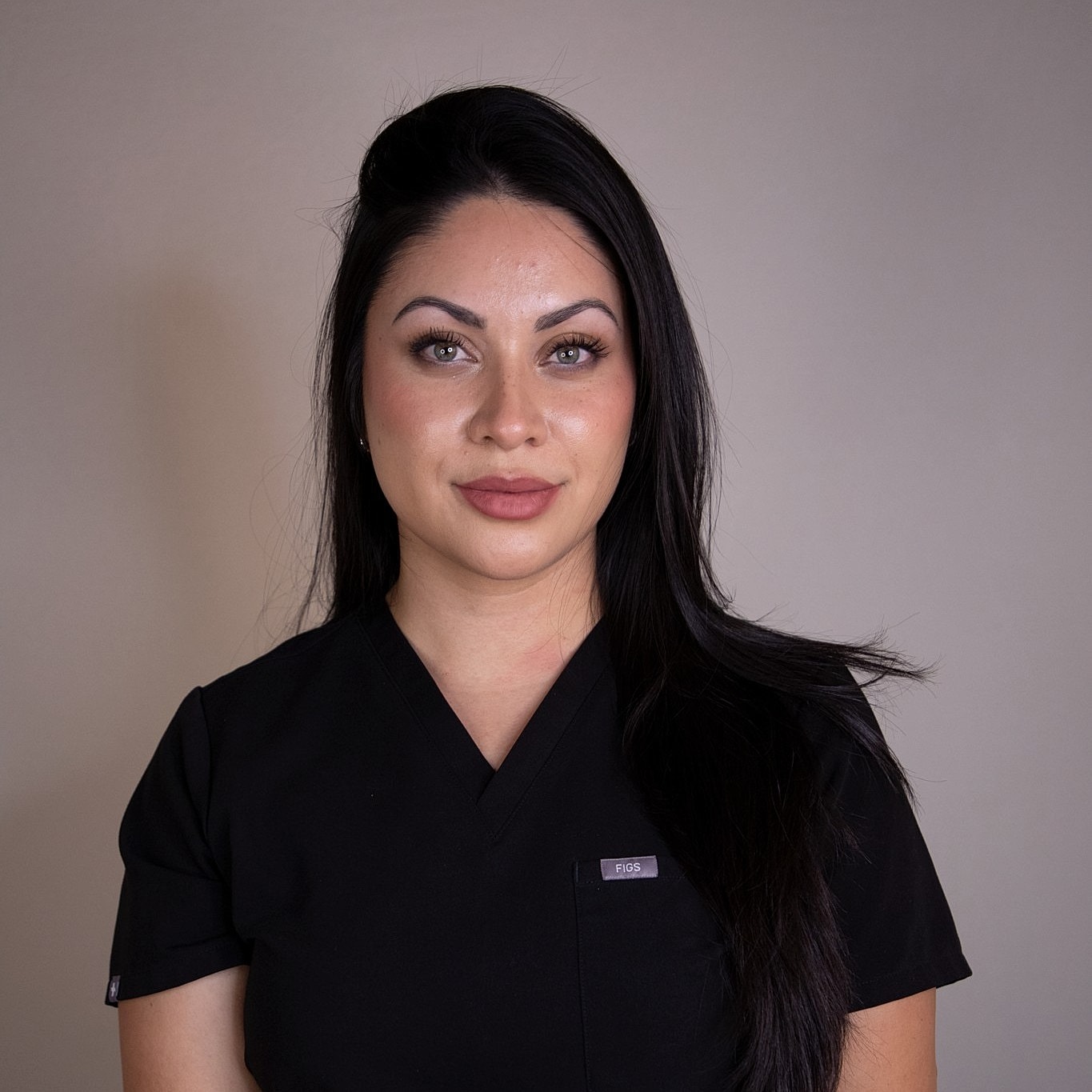 Woman in black scrubs posing against white background.