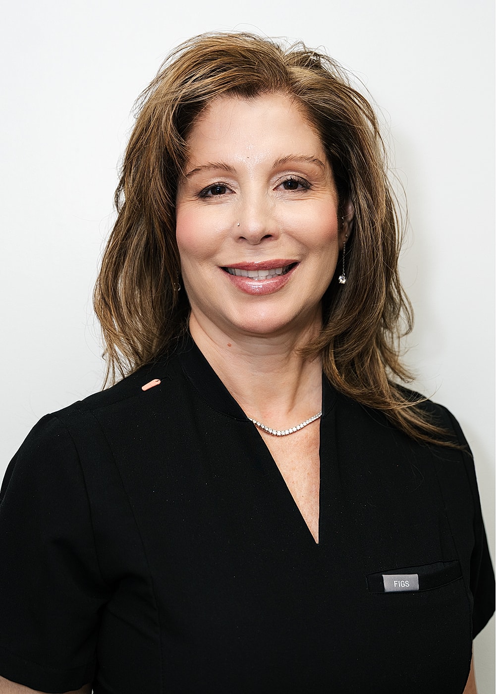 Smiling woman in medical scrubs against white background.
