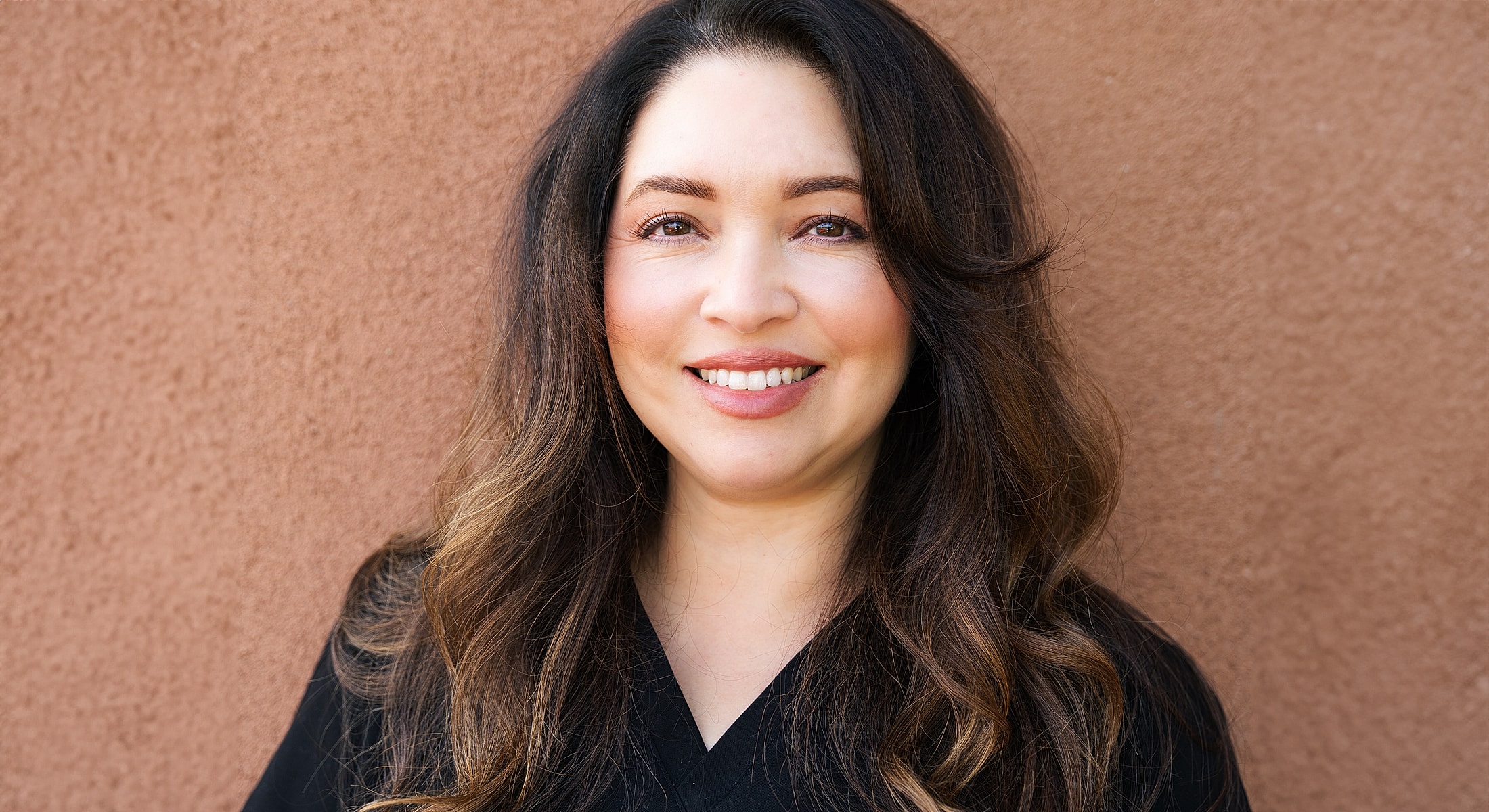 Smiling woman with long hair against a wall.