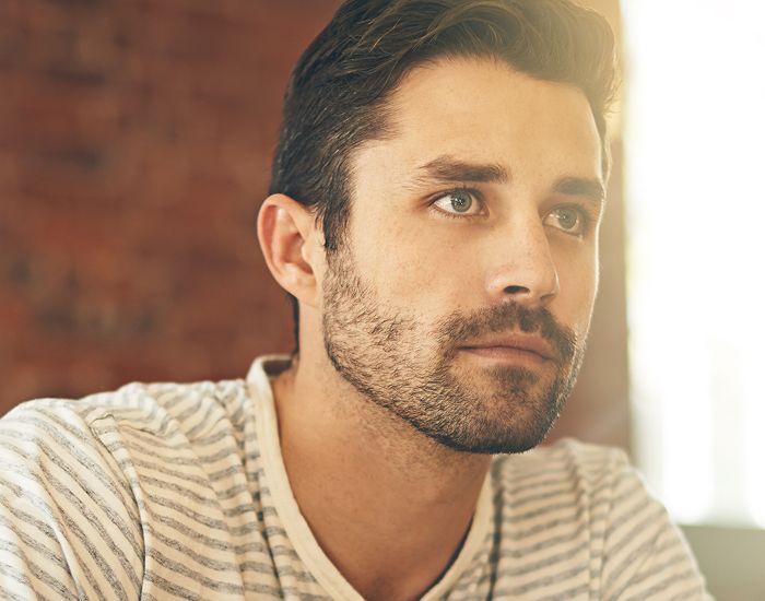 Man with thoughtful expression against brick background.
