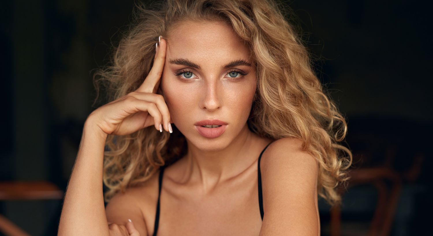 Santa Fe Ultherapy model with curly hair posing thoughtfully indoors.